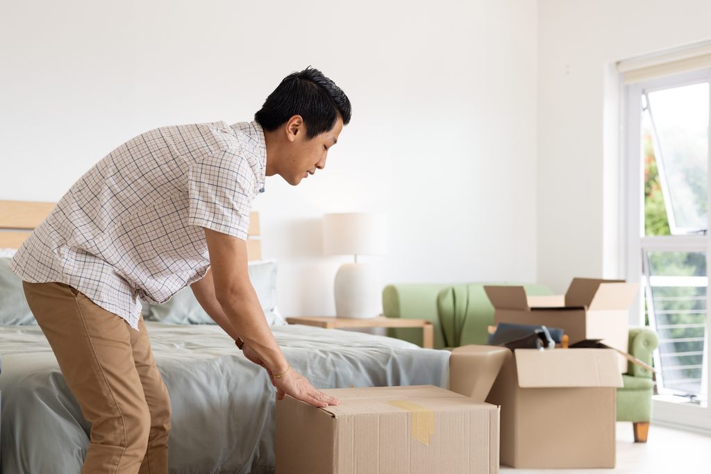 A man unpacking boxes in a sunlit bedroom.