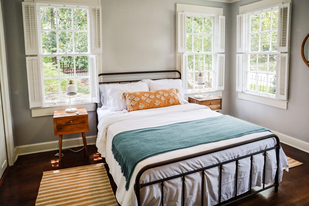 A spare bedroom with the bed made and light from two windows.